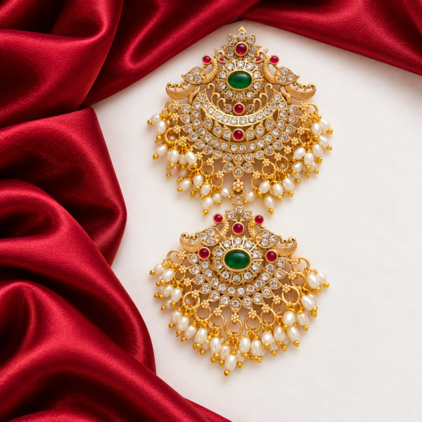 Gold-tone double peacock Jada Billa hair ornament with emerald-green centre stones, ruby-red accents, white stones and pearl-like bead drops.