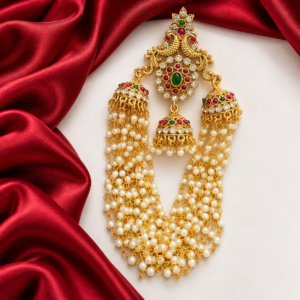 South Indian peacock jhumka bridal hair accessory with ruby green stones, three decorative jhumkas and layered white pearl chains.