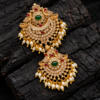 Double peacock Rakodi Jada Billa hair accessory with green centre stones, ruby-red accents, white stones and pearl-like bead drops on black wood.