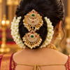 South Indian bride wearing double Rakodi Jada Billa with peacock design, ruby green stones and pearl drops on jasmine-decorated hair bun.